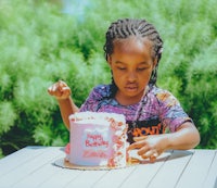 a little girl is sitting at a table with a birthday cake