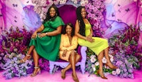 three women sitting on a purple chair in front of flowers