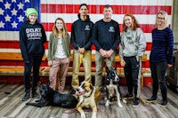 a group of people posing with their dogs in front of an american flag