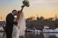 a bride and groom kiss in front of the water at sunset